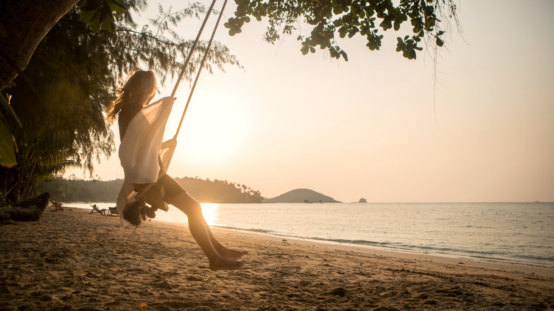 Frau auf einer Schaukel am Meer im Sonnenuntergang